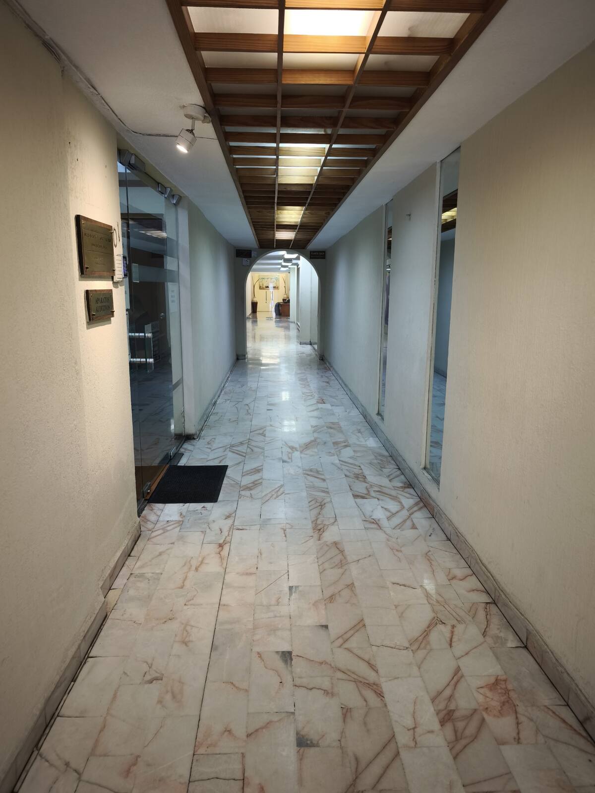 Pasillo de planta baja del Centro Médico Obispado: piso de mármol con vetas rosas, muros claros y plafón de madera en retícula